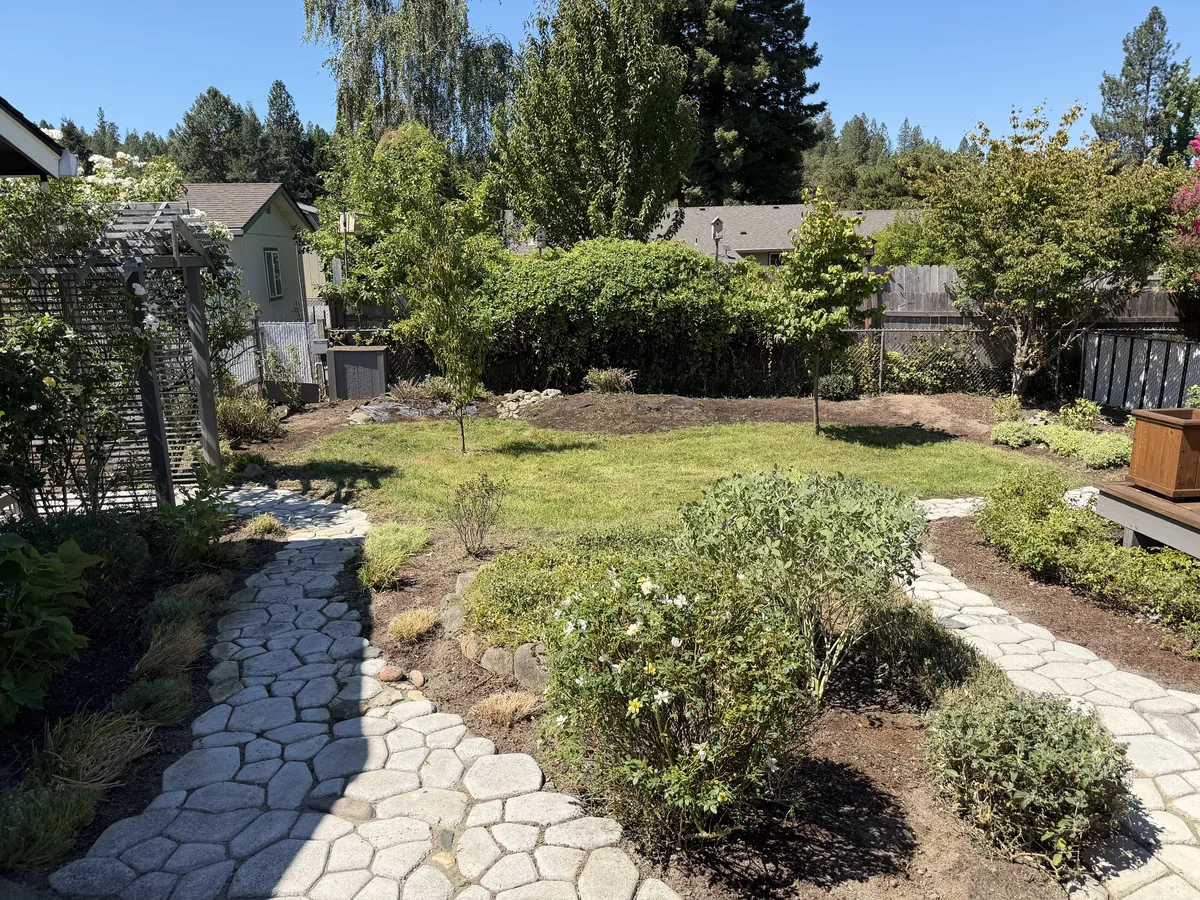 Backyard with fresh dark mulch in the planting beds, paver stone pathways, roses and young trees after a Peak cleanup in Southern Oregon