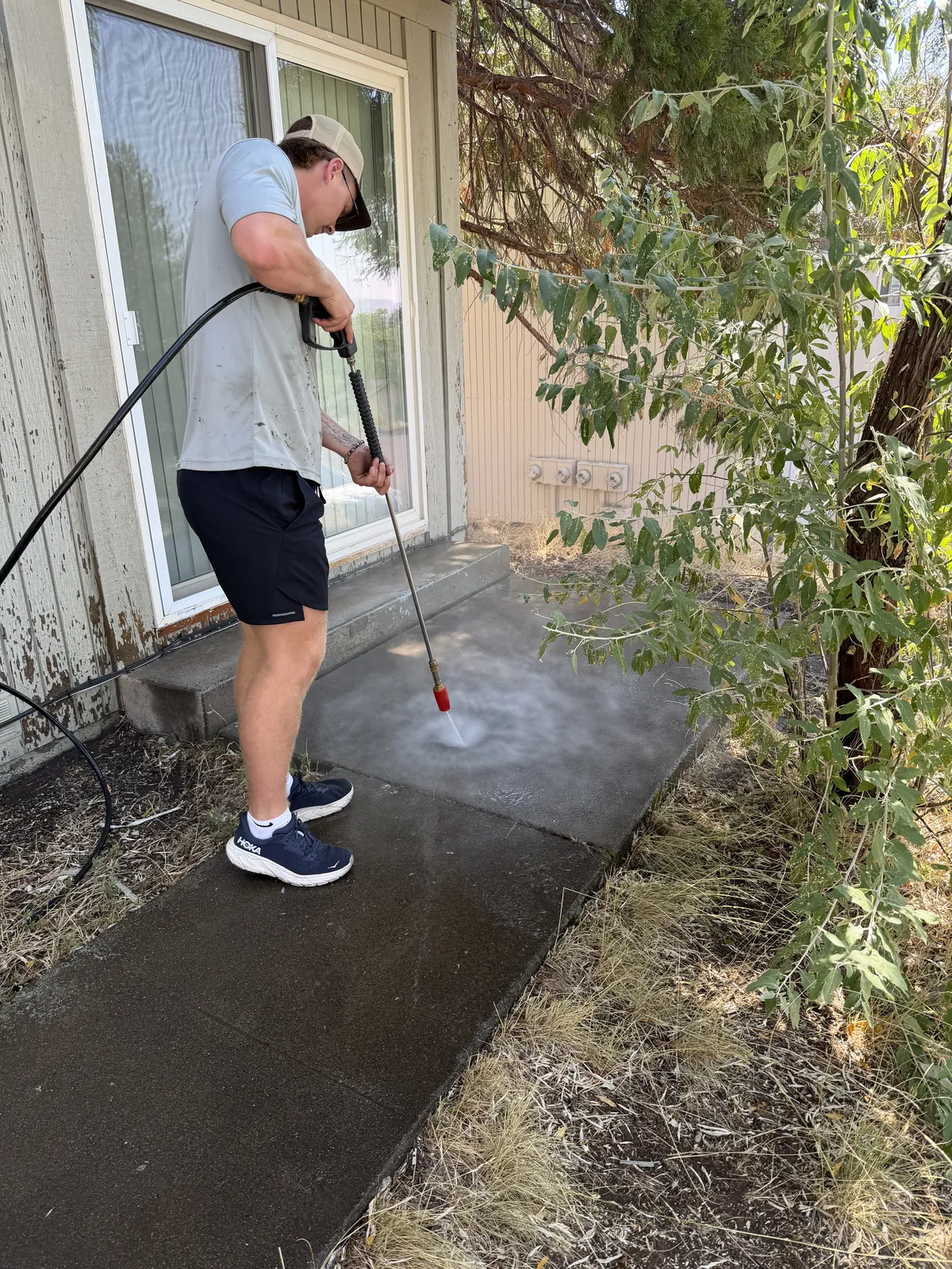 Peak Landscaping crew member pressure washing built-up grime off a concrete patio and walkway at a Southern Oregon home