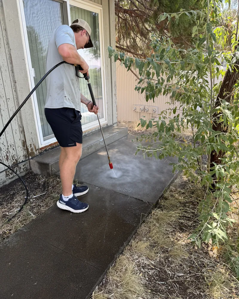 Peak Landscaping crew member pressure washing built-up grime off a concrete patio and walkway at a Southern Oregon home