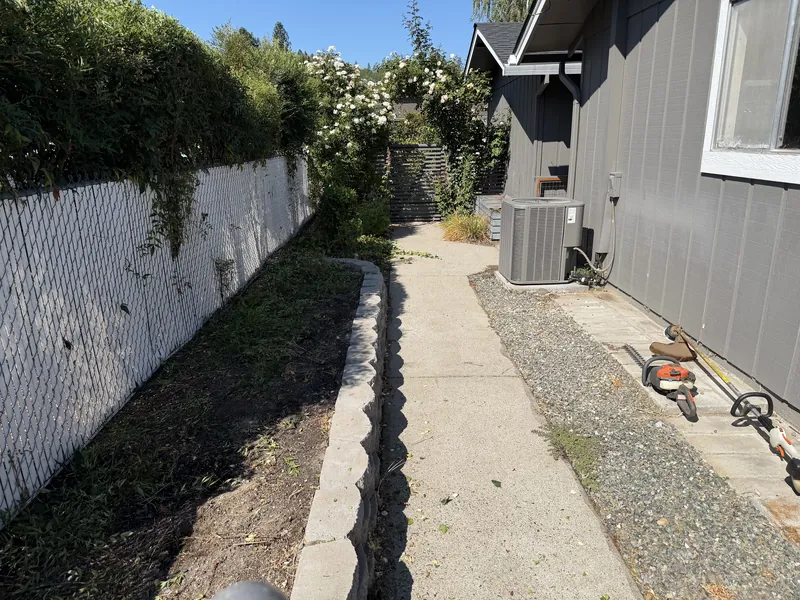 Weedy side yard planting bed along a chain link fence before Peak Landscaping cleared it, Southern Oregon